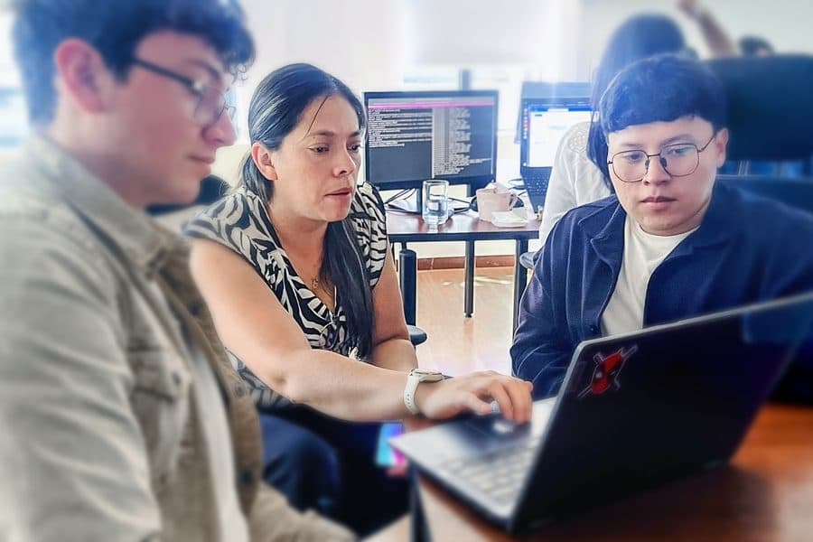 A Senirop engineer guiding two colleagues through a code review on a laptop at the Quito, Ecuador office