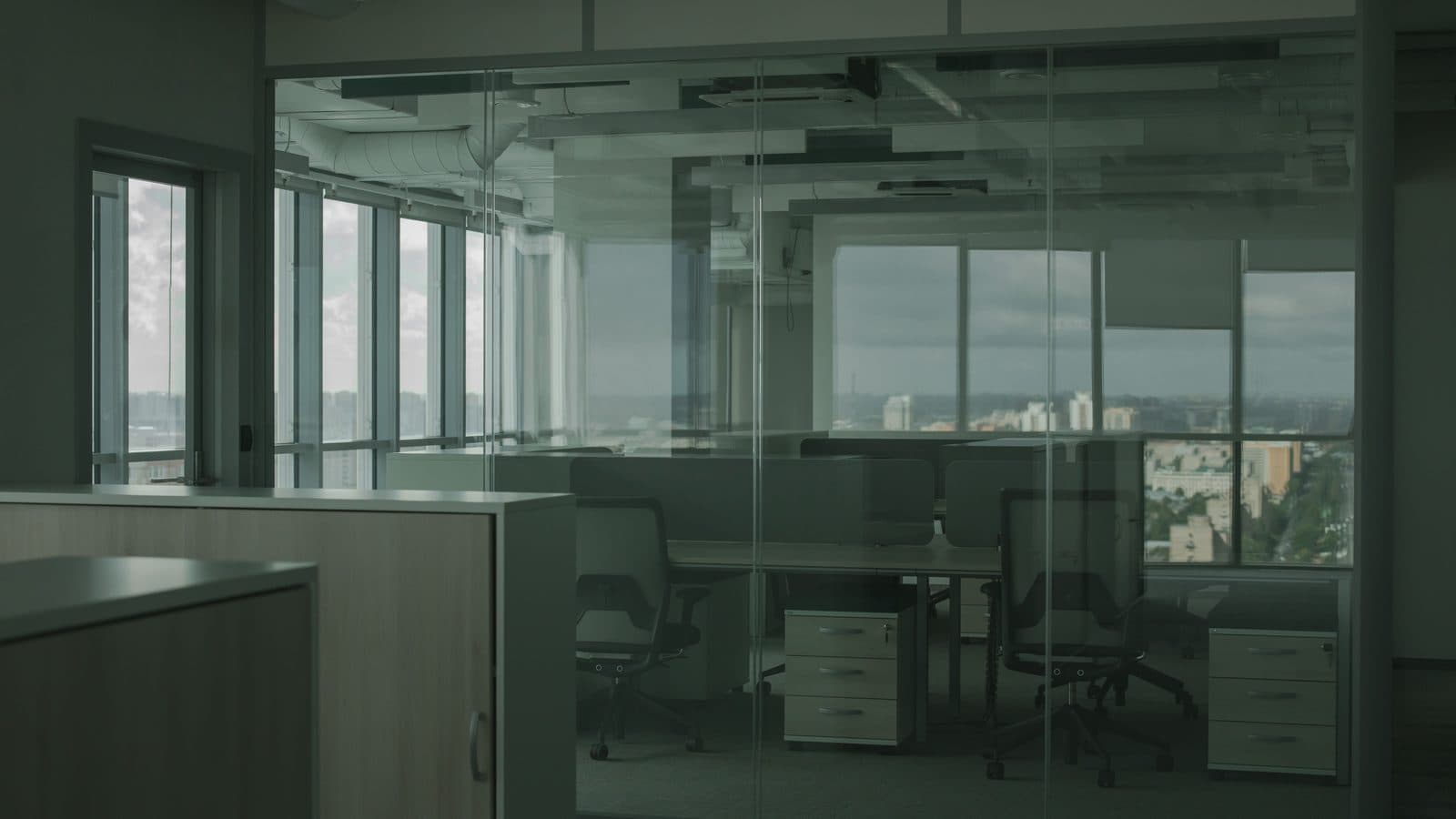 An open-plan office workspace behind glass partitions, overlooking a city skyline